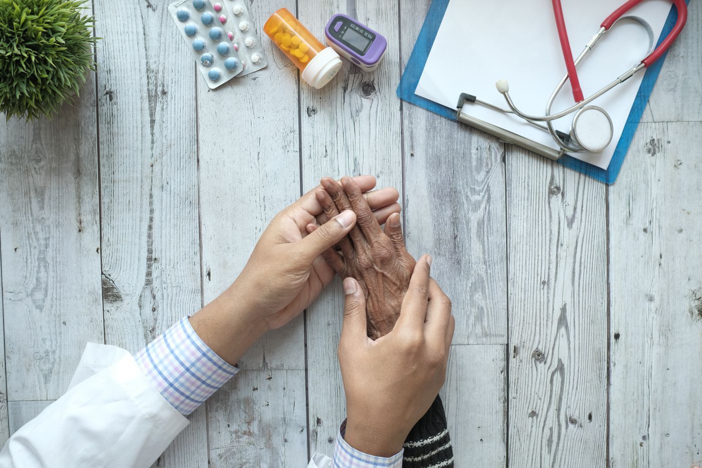A doctor's hands with a patient beside a stethoscope, clipboard, and medical tests on a desk